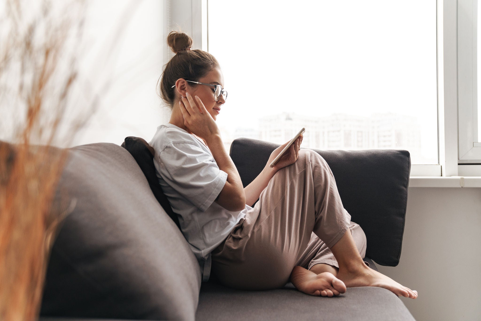a woman sitting on a couch near windows looking at her phone