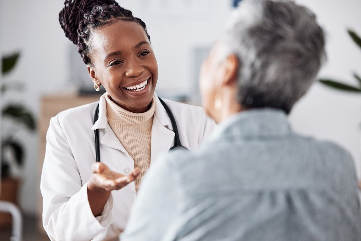 Smile, black woman or doctor consulting a patient in meeting in hospital for healthcare feedback or support. Happy, medical or nurse with a mature person talking or speaking of test results or advice.