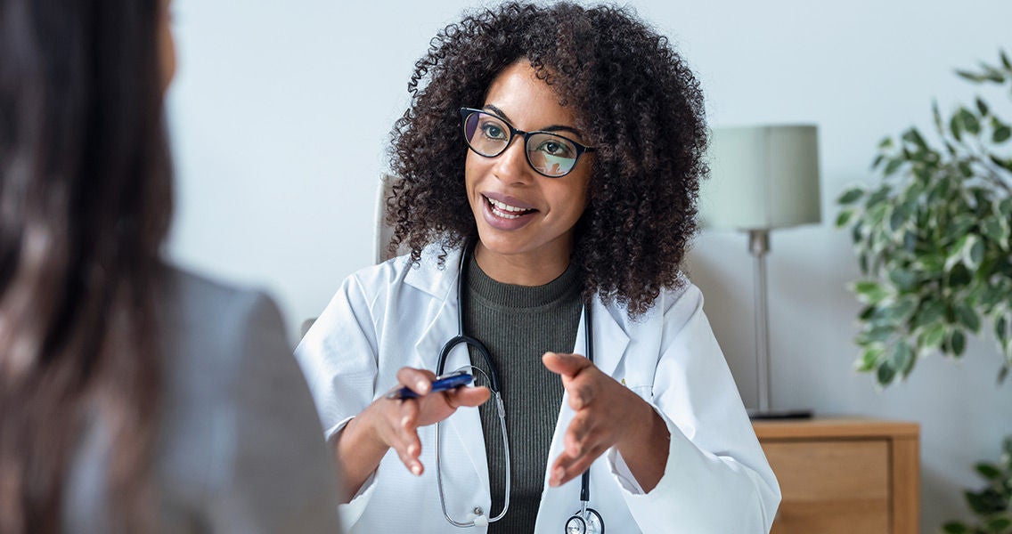 Doctor facing patient/camera talking at a desk smiling
