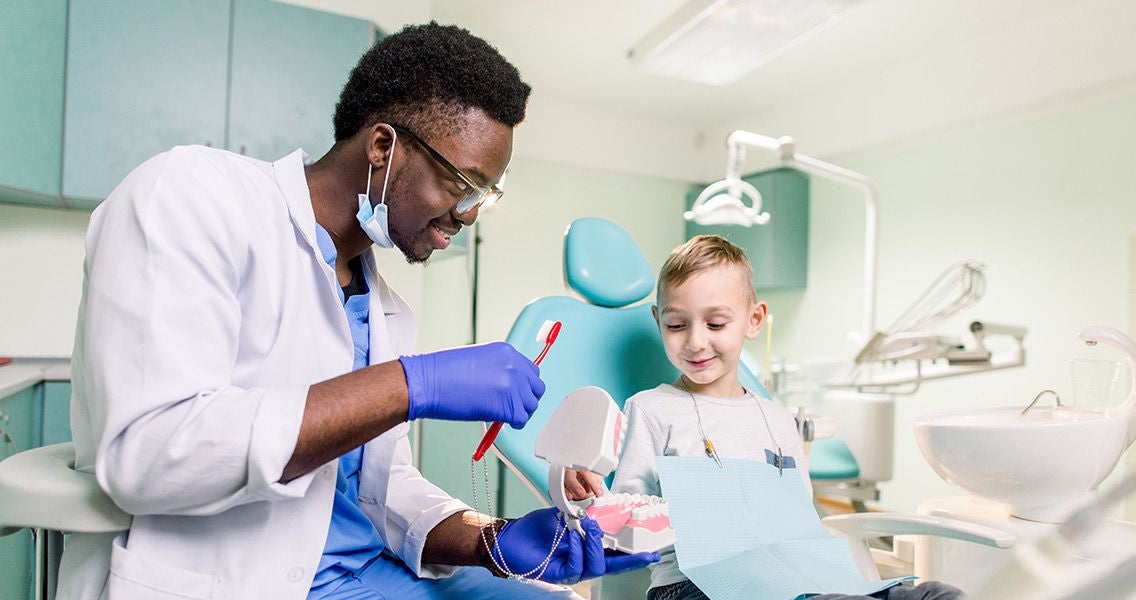 Dentist with a child at an appointment showing him how to floss