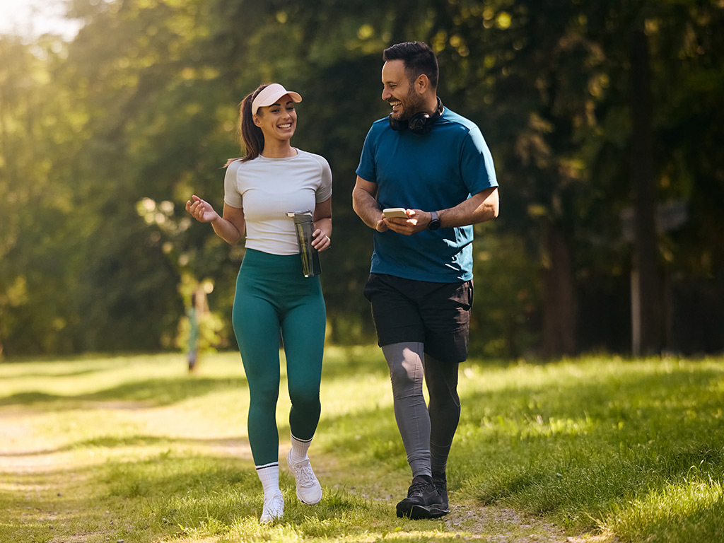 A woman and man dressed in athletic clothes are walking at a park. 