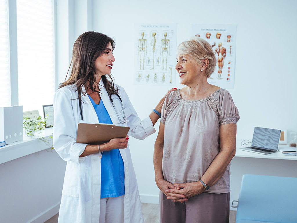 An older woman smiles as her doctor places a hand on the woman's shoulder.
