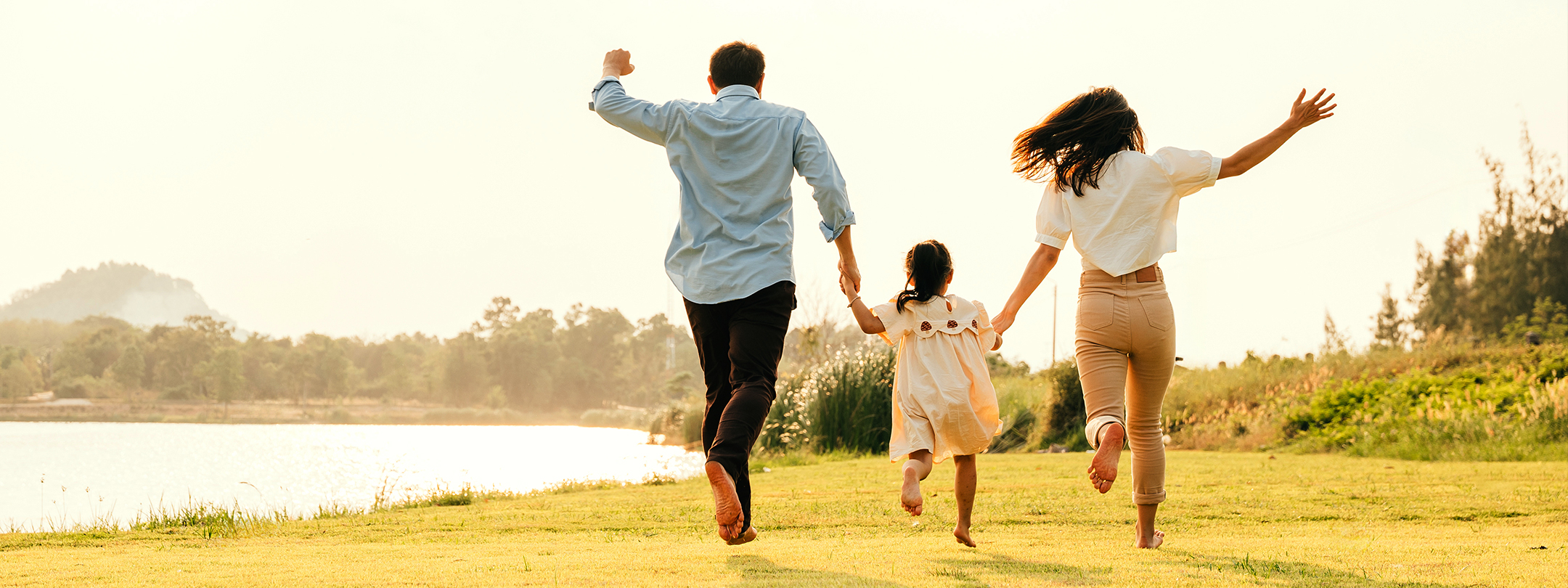 Joyful parents and child run outside near a pond