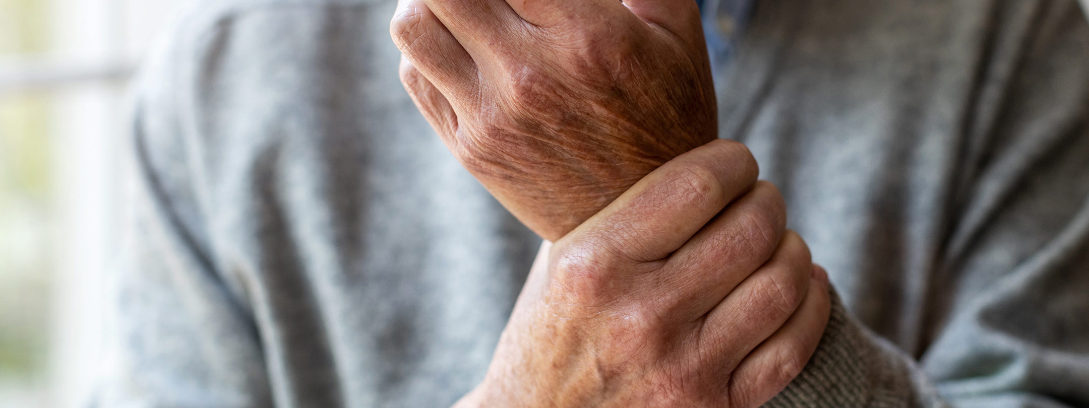 elderly person holds his wrist in his other hand