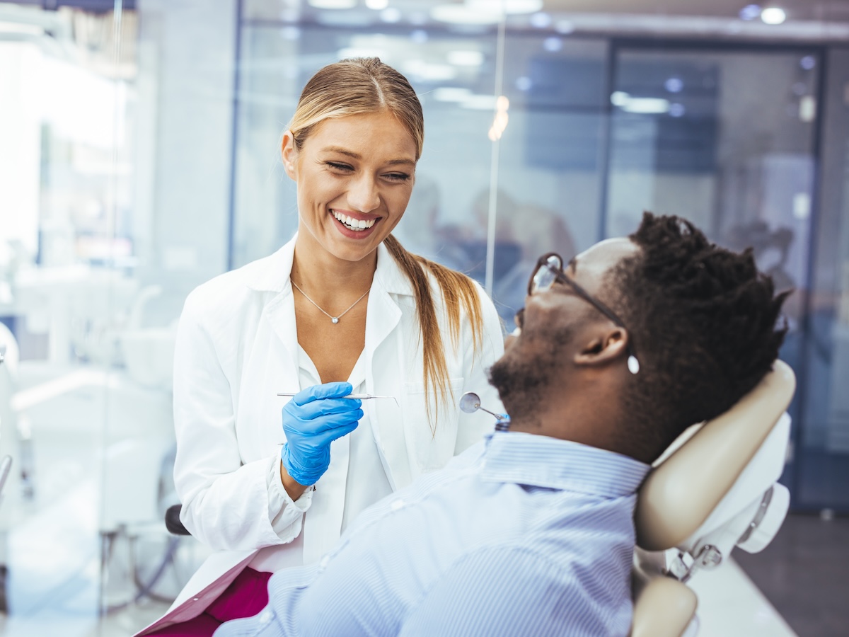 Young man patient having dental treatment at dentist's office. Female dentist working on patient's teeth. Man having teeth examined at dentists. Overview of dental caries prevention