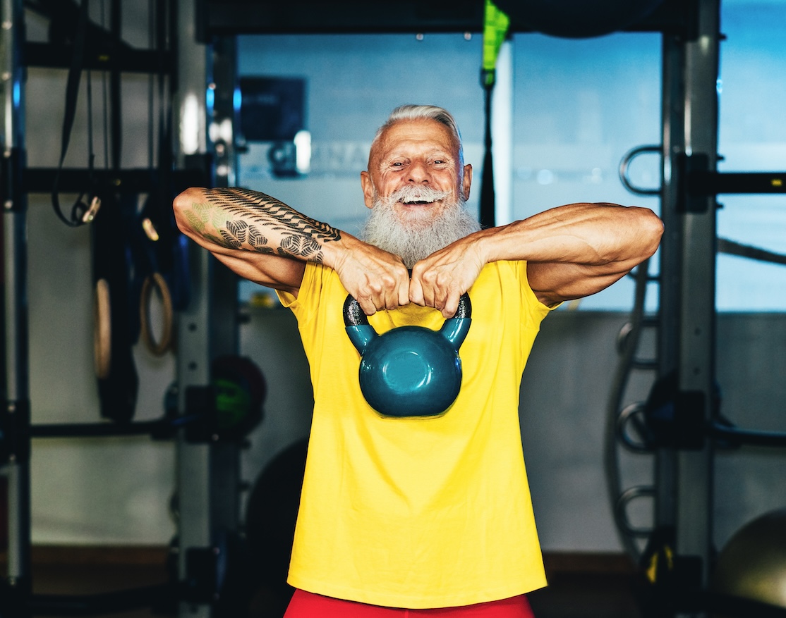 Hipster senior man training inside gym - Mature tattooed person having fun doing workout exercises in sport fitness club - Active joyful elderly lifestyle and fit concept - Focus on face