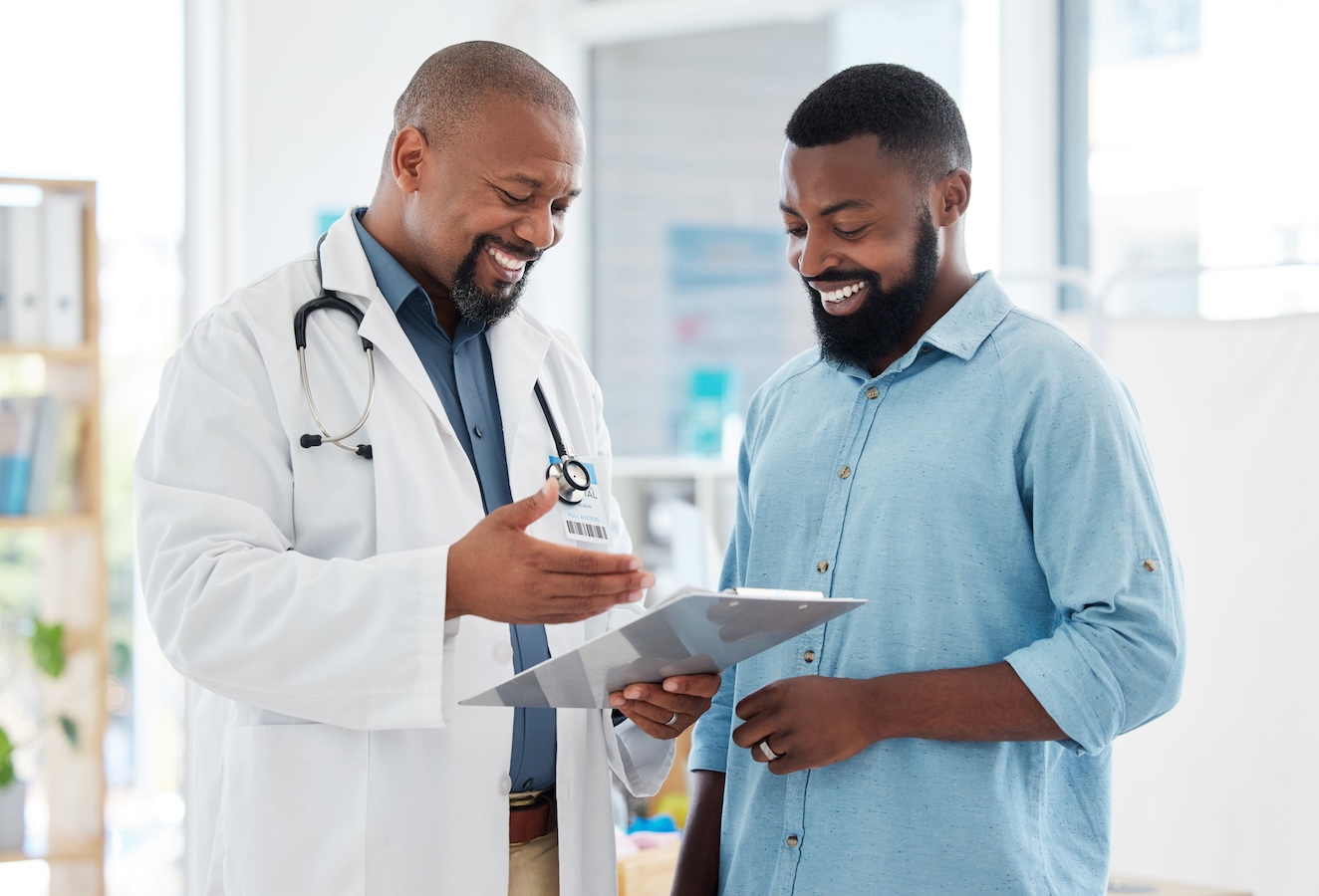 Healthcare, black man and doctor with clipboard, diagnosis and conversation for results, smile and care. Male patient, guy and medical professional with documents, paperwork for insurance and talking.