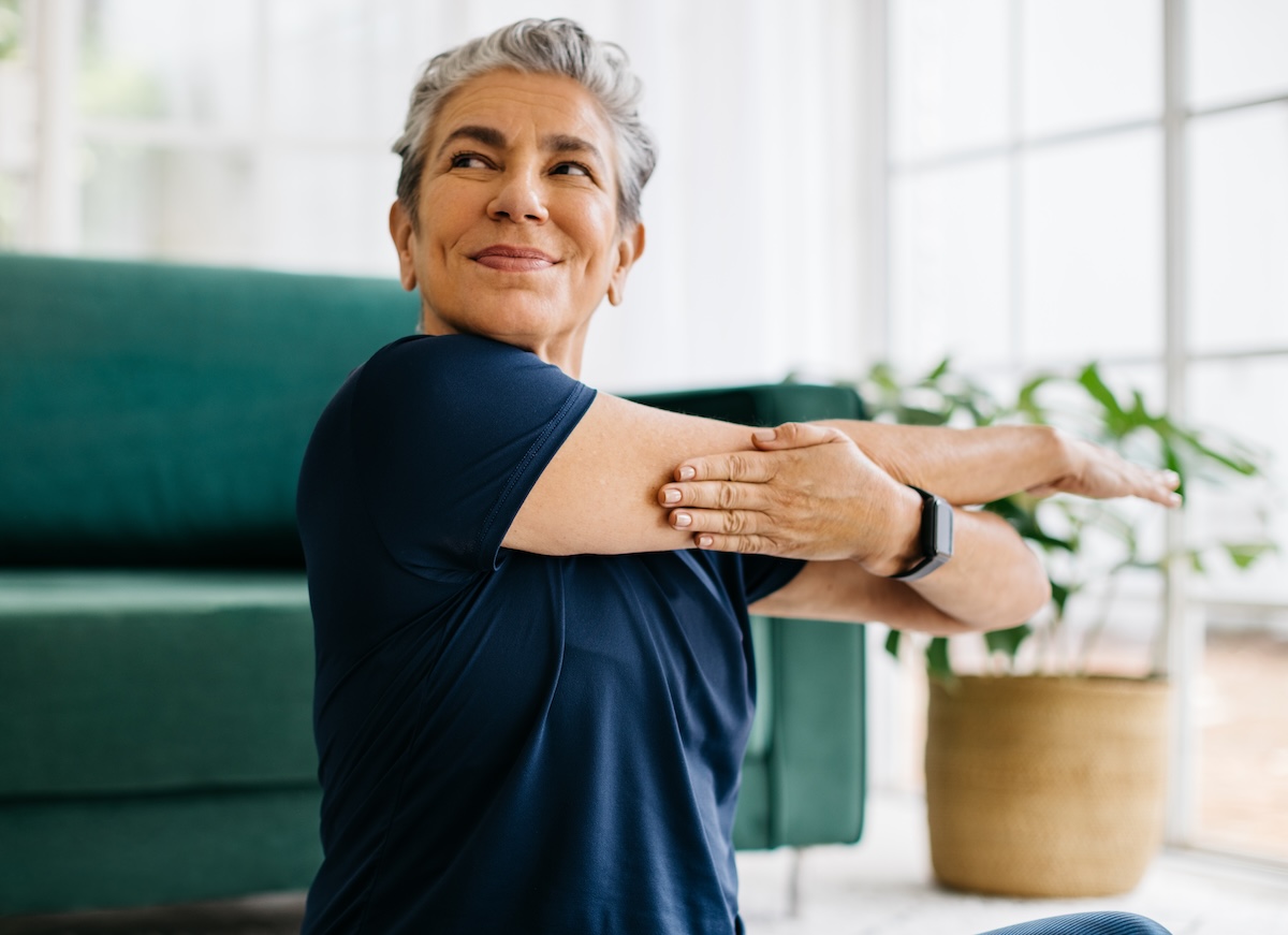 Happy and healthy senior woman doing a shoulder mobility exercise at home, working out with a cross arm stretch in her yoga session. This mature woman is keeping herself active with a fitness routine, maintaining physical wellbeing and wellness as she ages.
