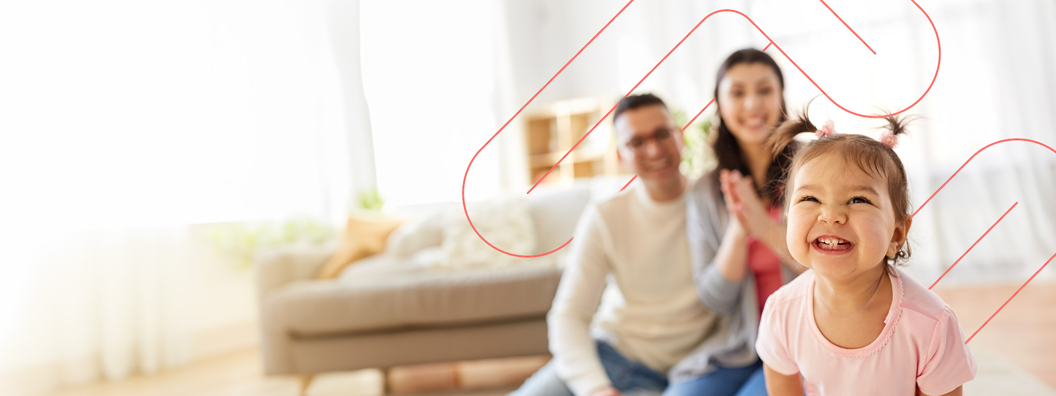 Toddler smiling at camera with parents in the background, in their living room
