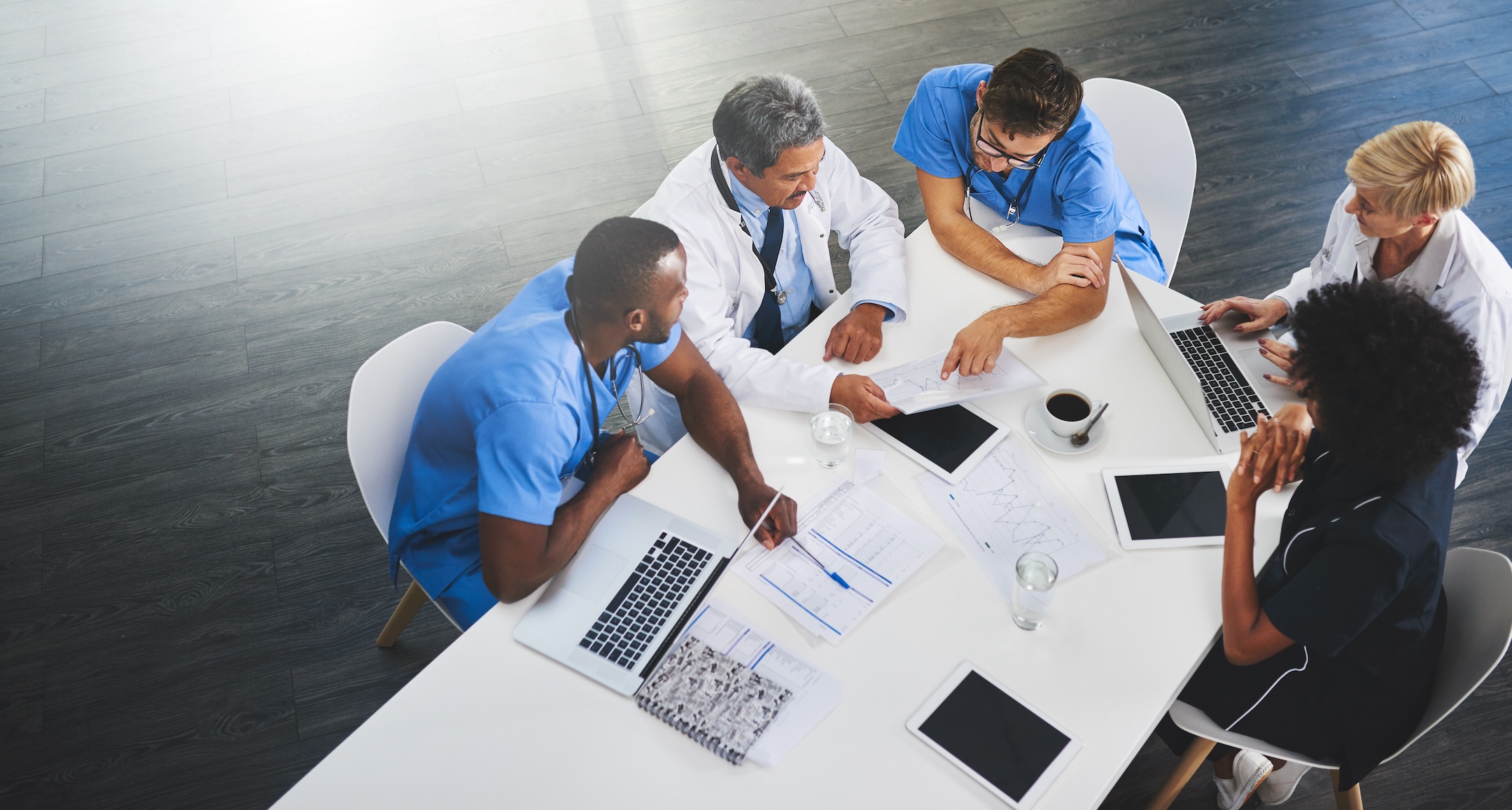 Team of medical workers sitting and meeting with laptops around table. Doctors and staff discussing papers and test results. Healthcare experts handling daily tasks and duties.