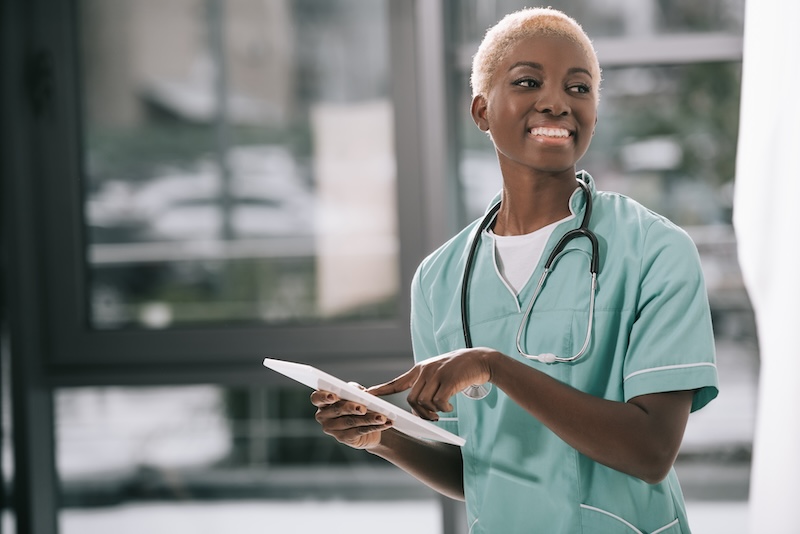 Smiling woman with stethoscope using digital tablet in clinic 