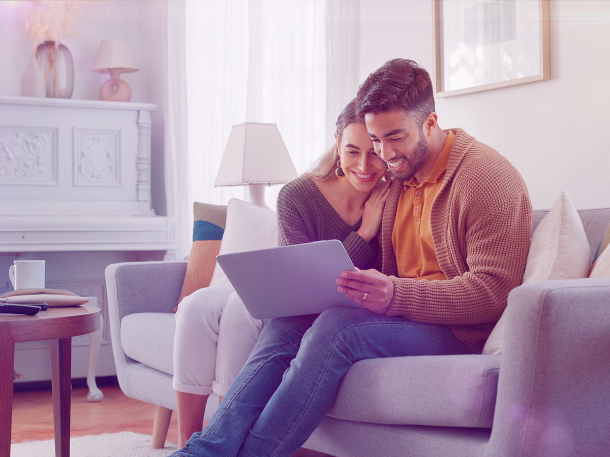 A photo of a young couple sitting on their couch looking at their laptop computer