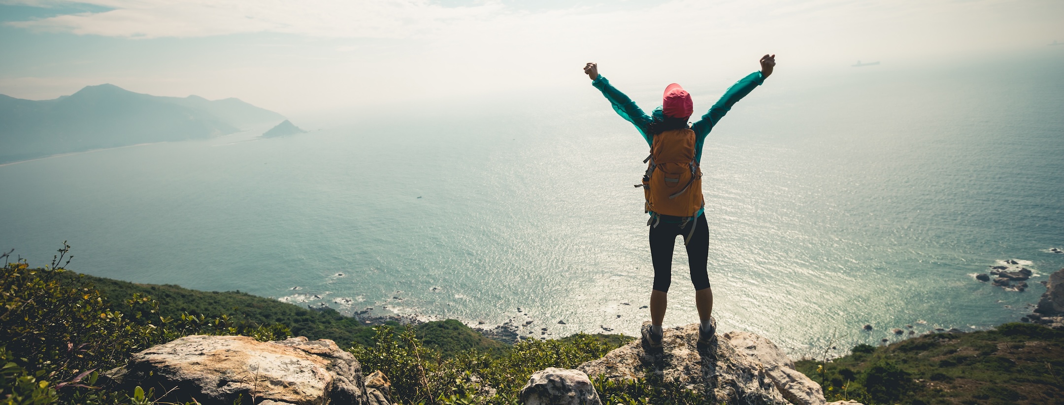 Successful hiker outstretched arms at seaside mountain top cliff edge