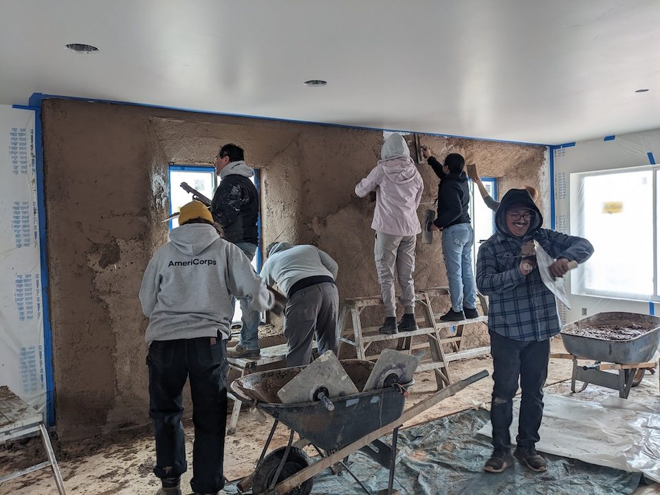 Team of volunteer construction workers applying drywall mud to a wall
